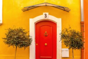 Image of a red door surrounded by yellow walls and two green trees